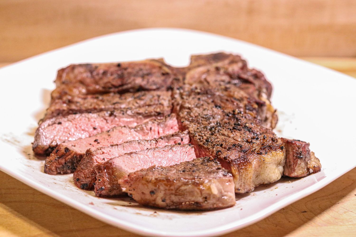 Raw ribeye steak on white plate with potato, rosemary, mushroom, asparagus, and butter on wooden cutting board.