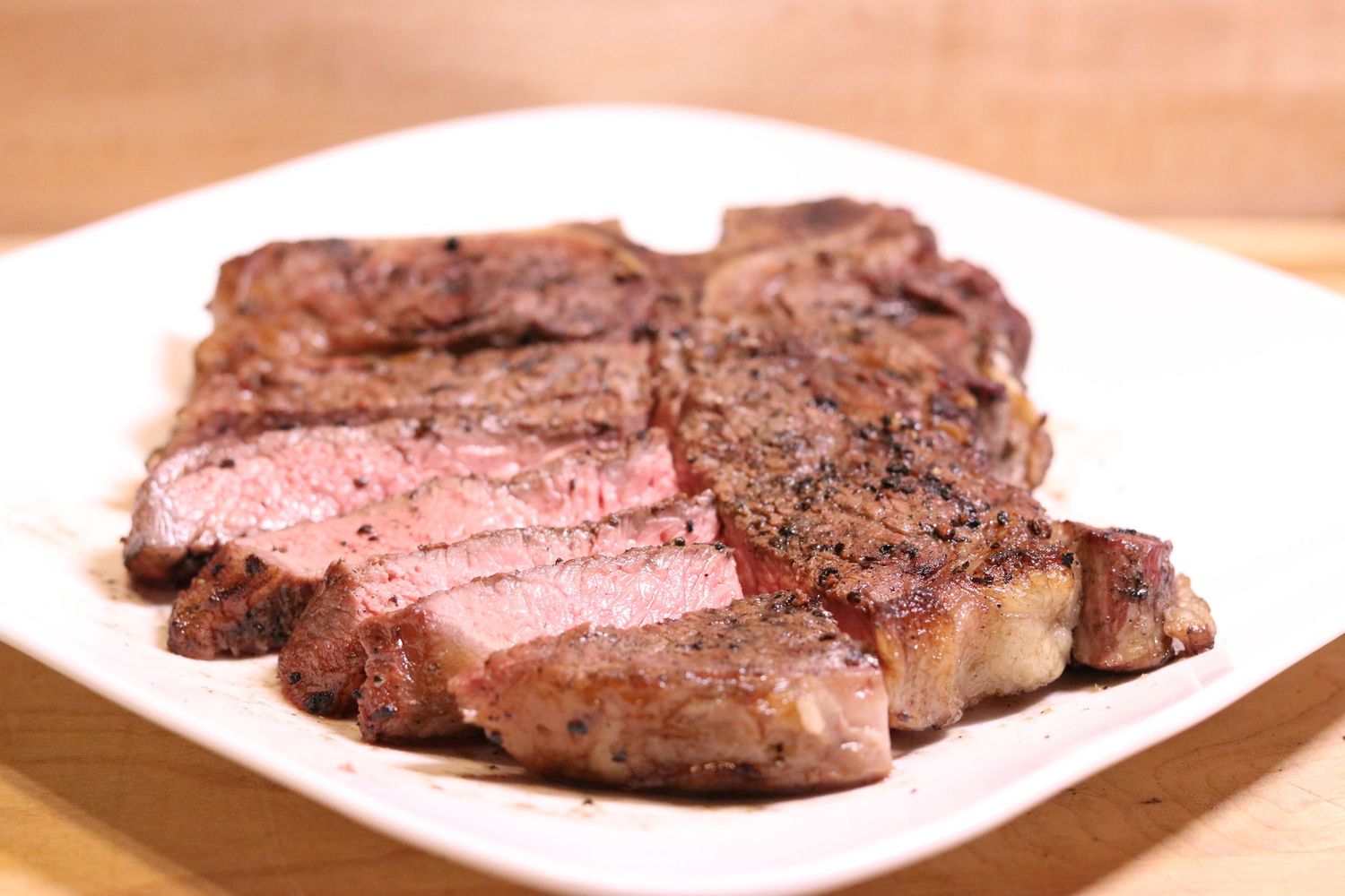 Juicy sliced T-bone steak cooked medium-rare served on a white plate, showing a perfect pink center.