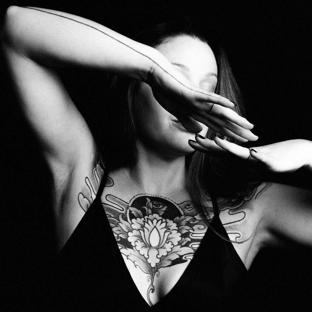 Portrait studio en noir et blanc mettant en valeur les tatouages et les jeux d'ombre.