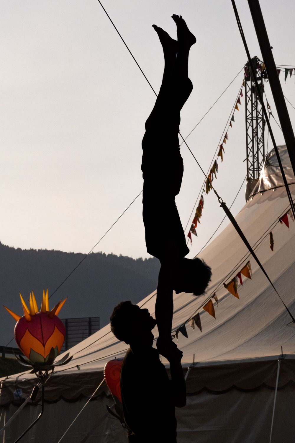 Duo d'acrobates réalisant un porté en silhouette devant un chapiteau.