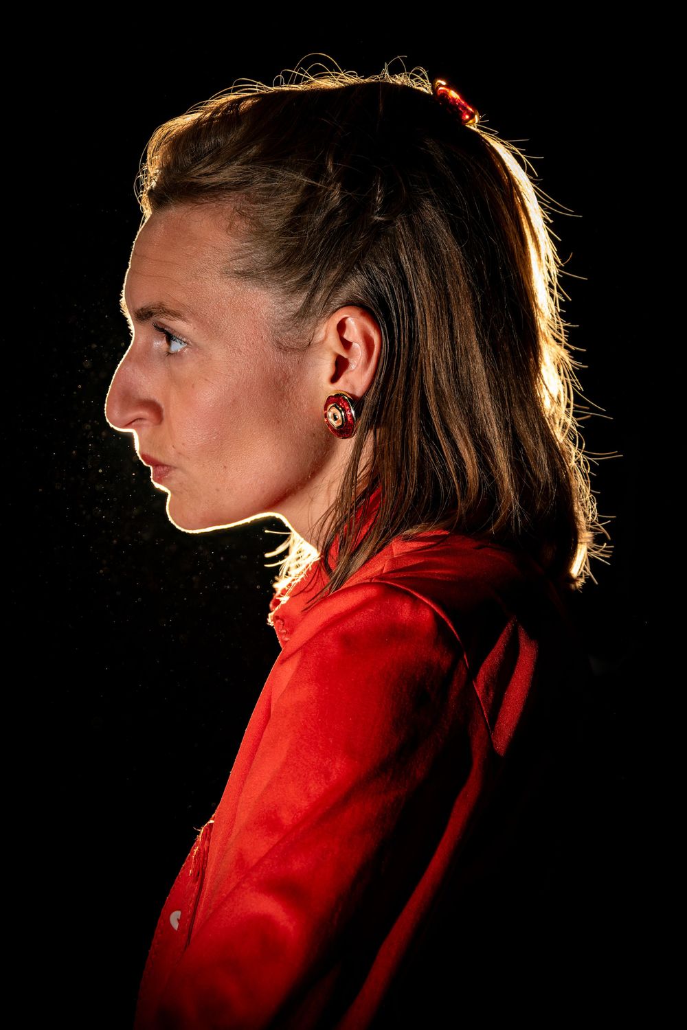 Comédienne en costume rouge éclairée en contre-jour sur une scène de théâtre.