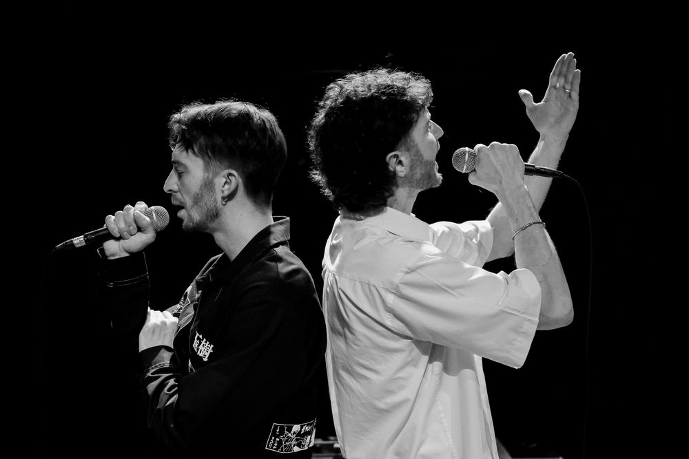 Deux chanteurs interprétant un morceau sur scène lors d'un concert en noir et blanc.