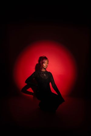 A woman in a black dress poses against a dramatic red circular light on a dark background.