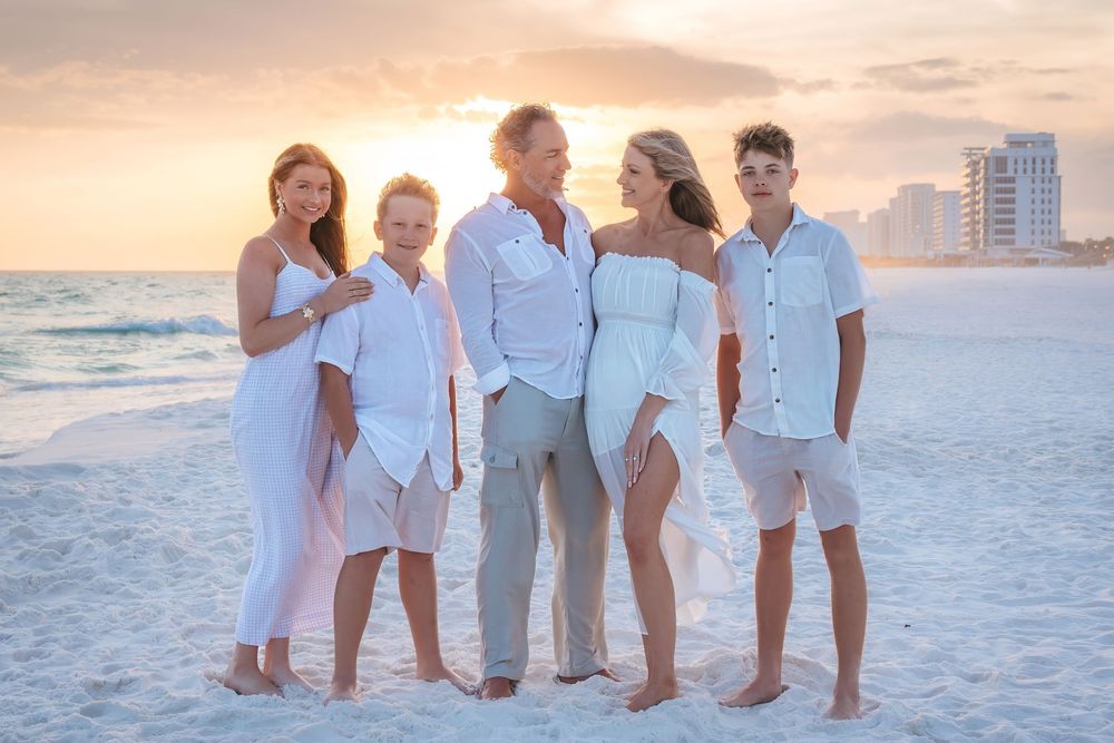 Family of five posing on beach at golden sunset, dressed in coordinating white and neutral outfits.