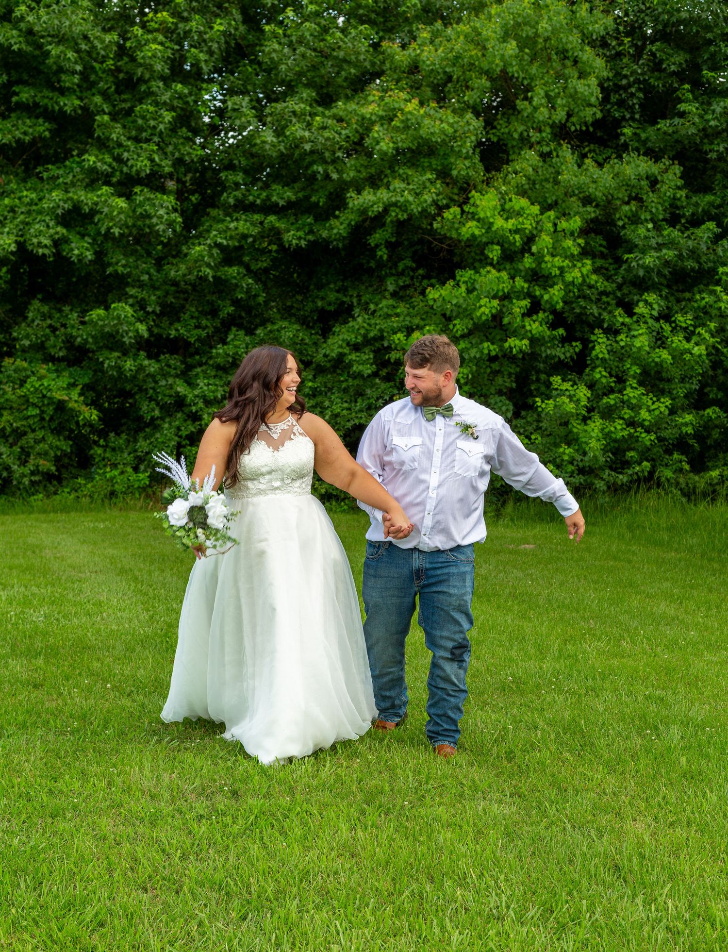 Bride and groom share first kiss at wedding ceremony aisle, bride holding white bouquet, guests seated in decorated venue.