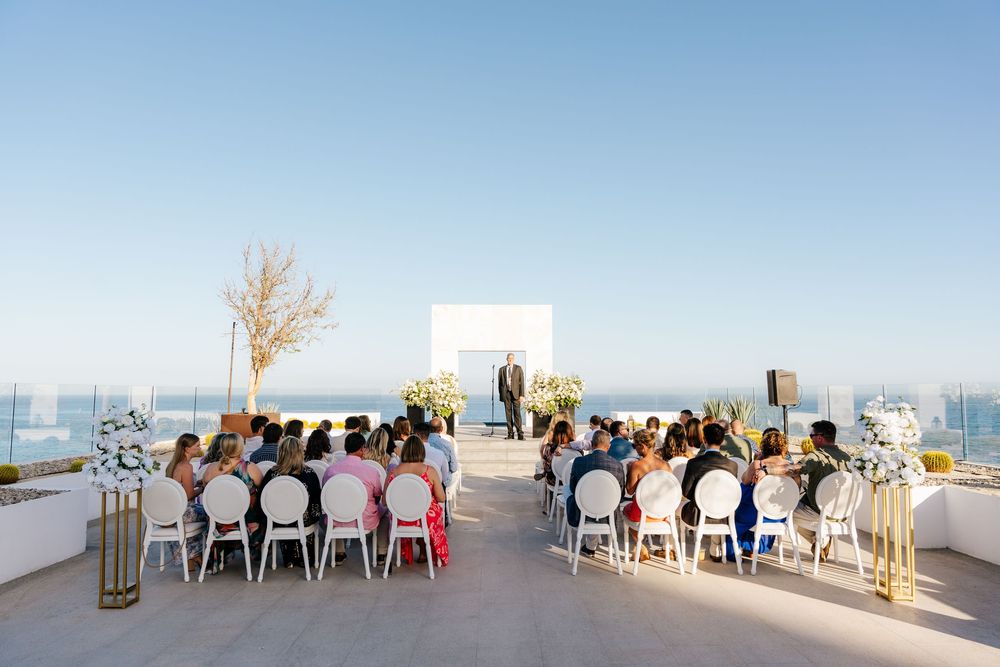 Outdoor rooftop wedding ceremony with ocean views, white chairs, and guests seated facing the altar.