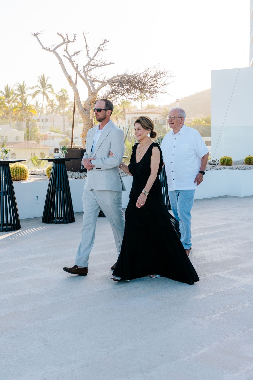 Elegantly dressed guests walk on a rooftop terrace at a wedding event in a tropical setting.