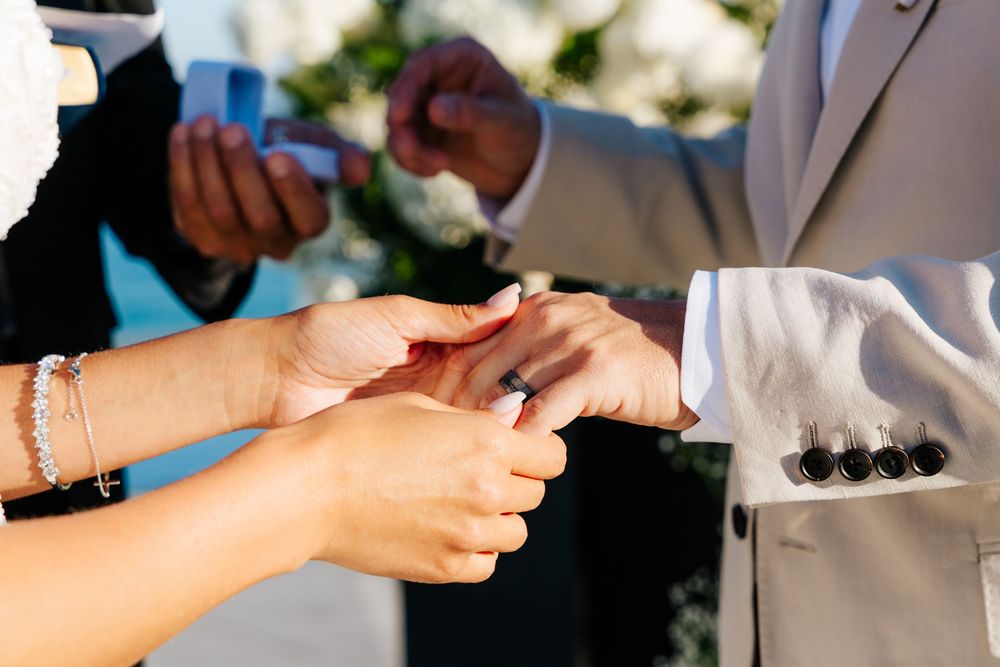 Close-up of wedding ring exchange with bride and groom hands during outdoor ceremony.