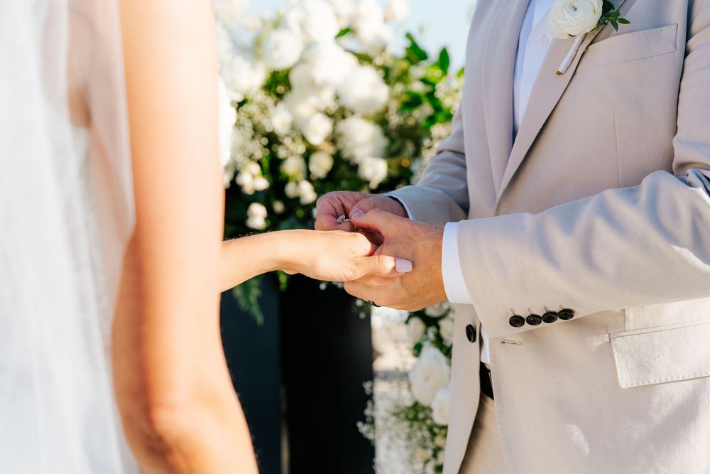 Bride and groom holding hands during outdoor wedding ceremony with white floral backdrop.