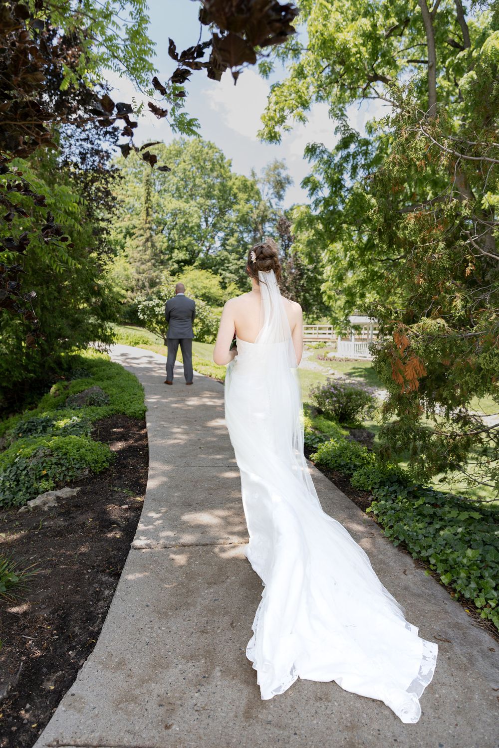 Bride walks toward dad for a first look on a path surrounded by greenery at the civic garden complex in london, ontario.
