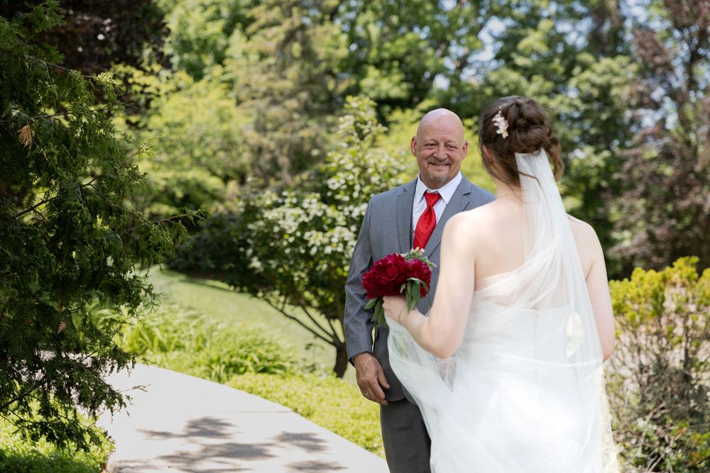 Bride faces smiling father on garden pathway during first look at the civic garden complex in london, ontario wedding.