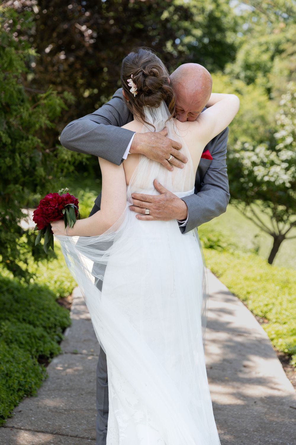 Bride and father share an emotional embrace on a garden path during a first look at the civic garden complex in london, ontario.