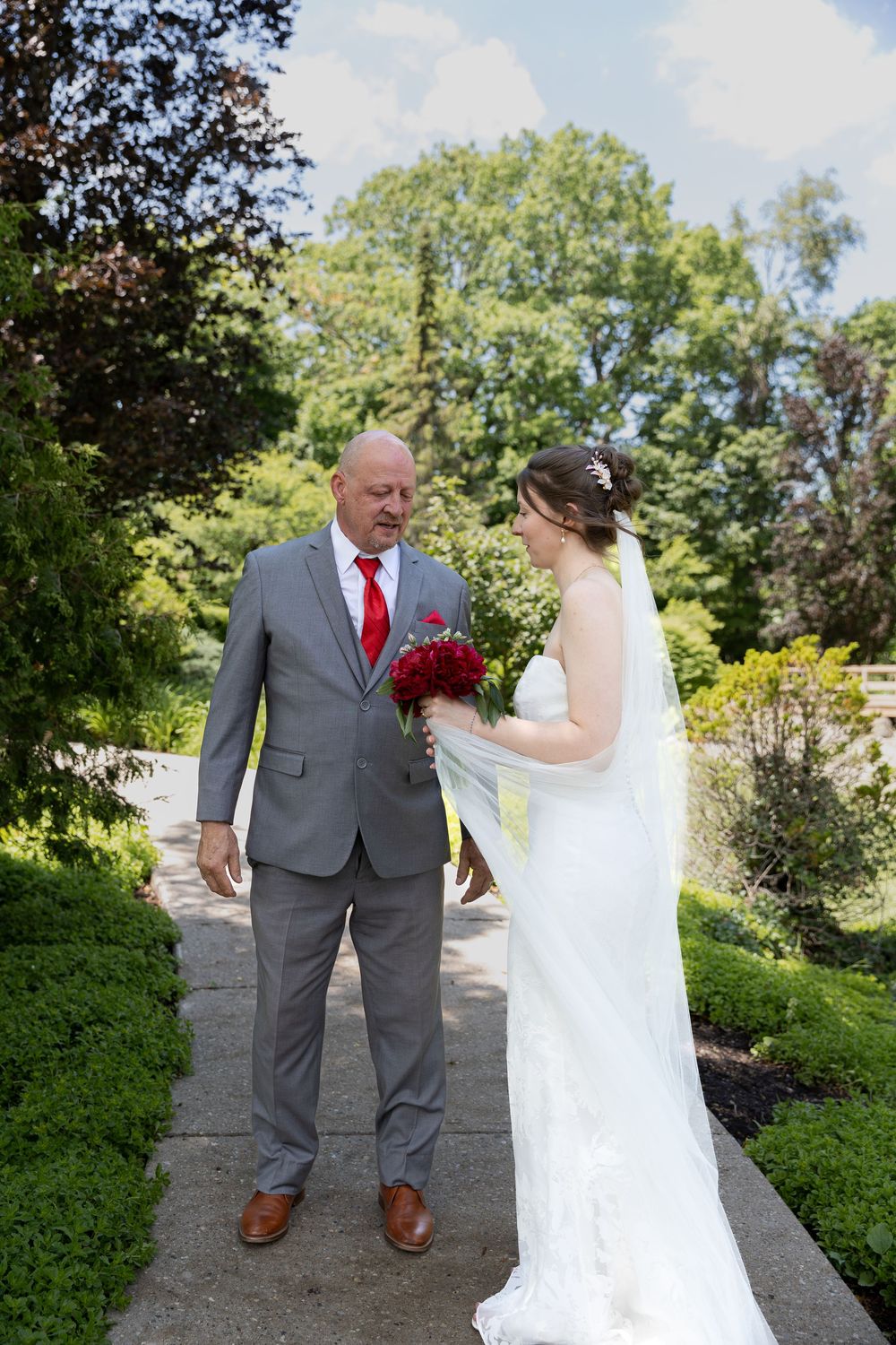 Bride in white gown holding red bouquet shares first look moment with father at the civic garden complex in london, ontario wedding.