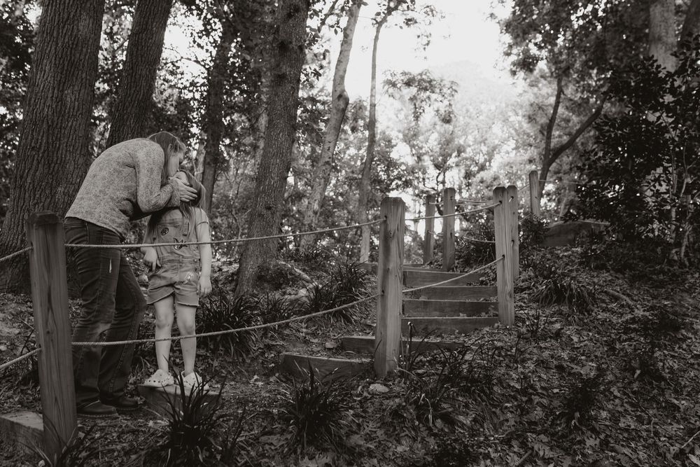 Mother kissing daughter on forehead in forest, black and white photography.