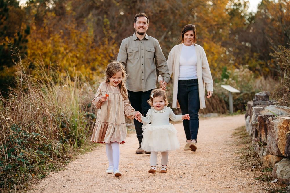 Young family of four walking together on a dirt path surrounded by autumn foliage.