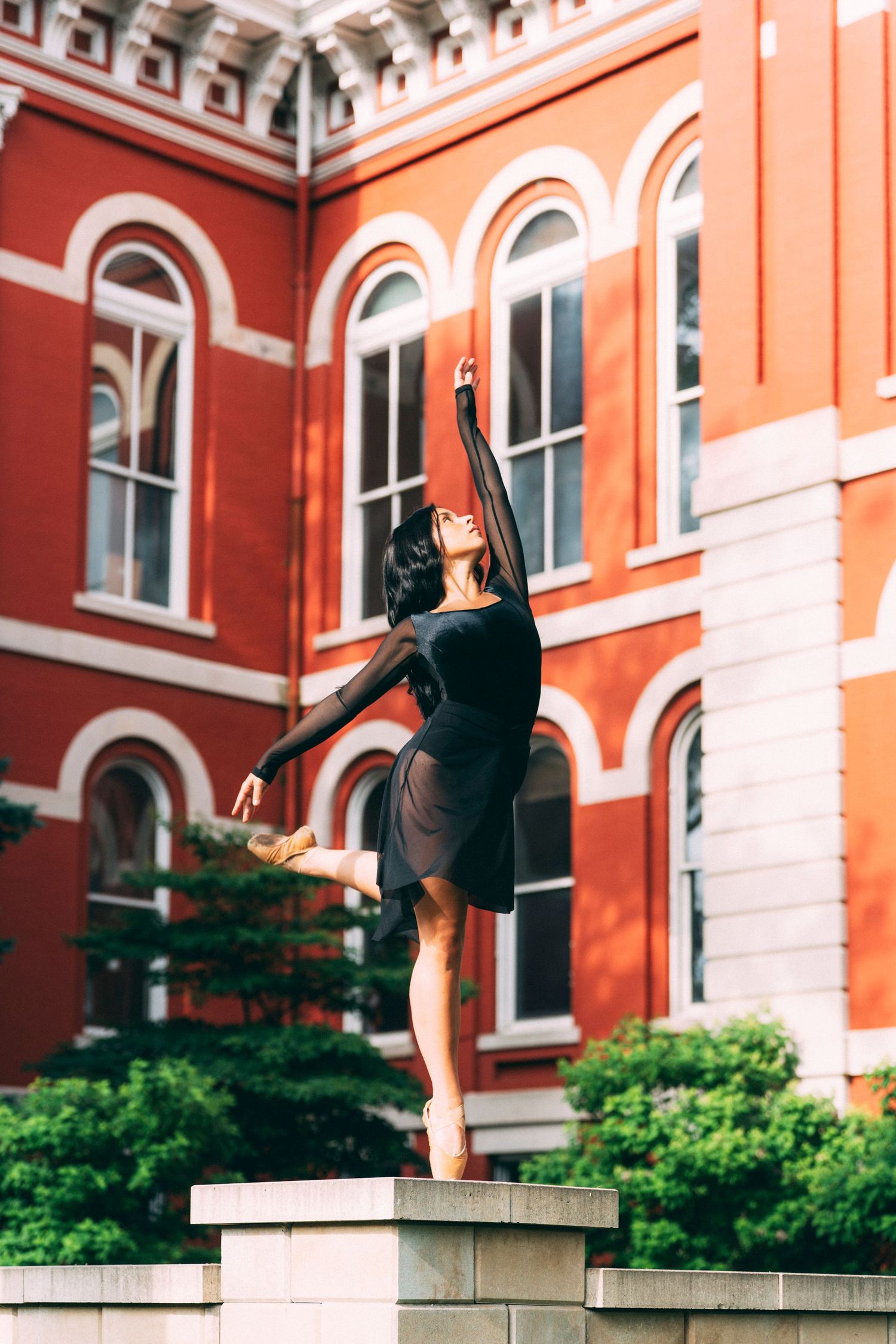 Senior portrait photographer closes professional dancer's Crown Point session in sheer black dress against courthouse brick.