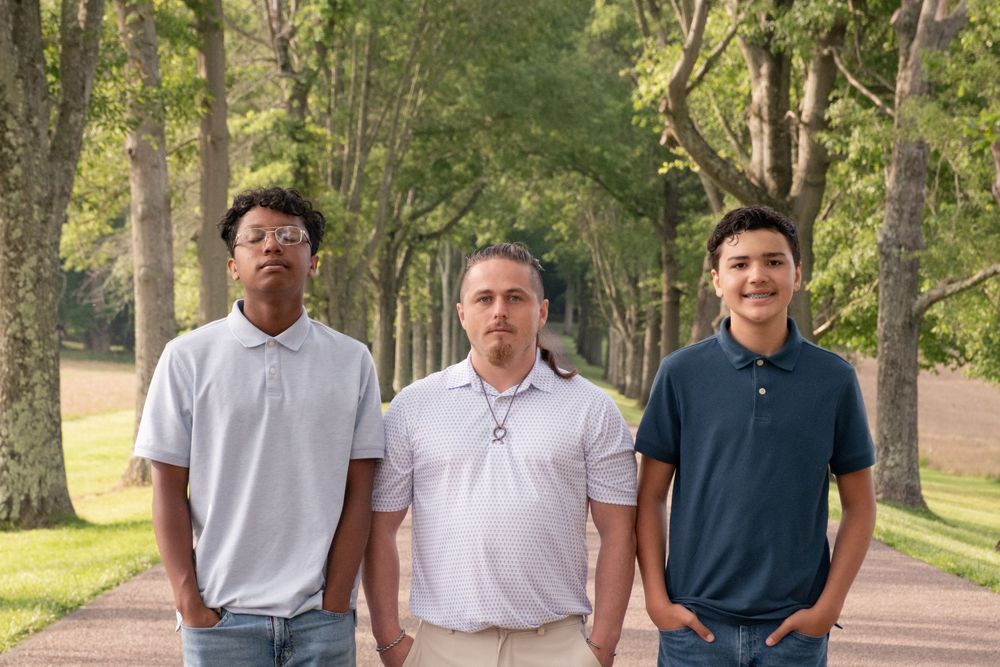 Three men standing on a tree-lined path in a park, wearing polo shirts and smiling at the camera. Uniontown, PA