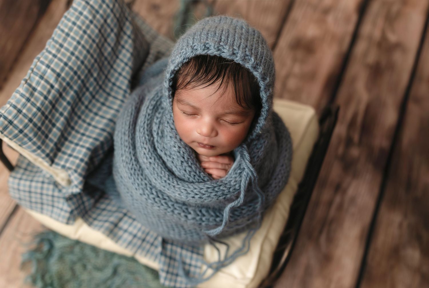 Baby boy wrapped in blue sleeps on a bed with a plaid pillowcase, captured by Charlottesville family and newborn photographer.