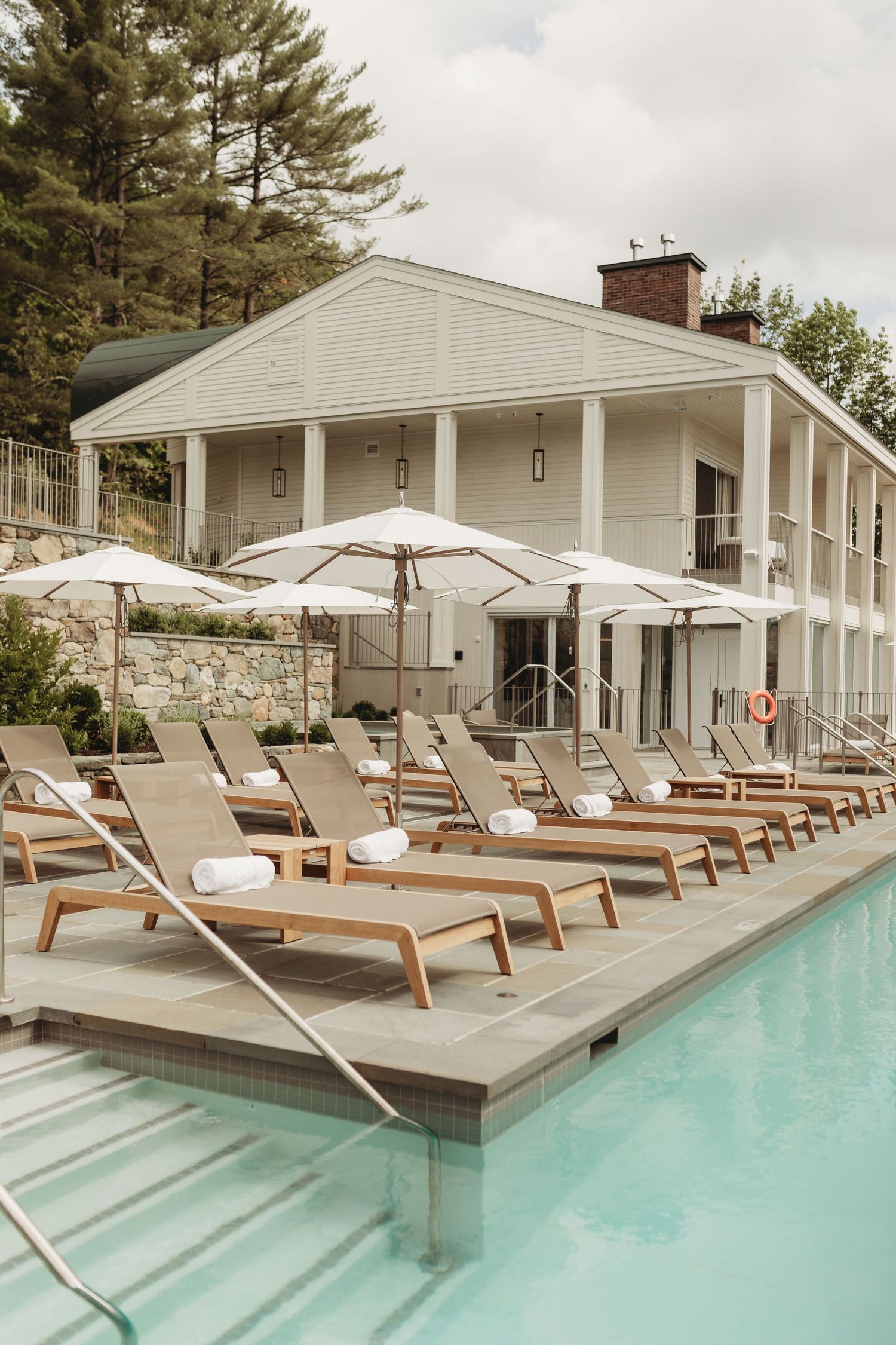 Luxury resort pool with lounge chairs, white umbrellas, and a classic white colonial building surrounded by trees.