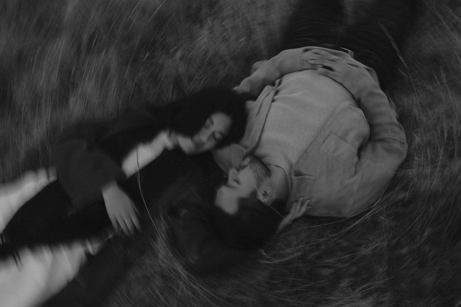 Black and white photo of two people lying on grass, captured from above in a dreamy, blurred artistic style.