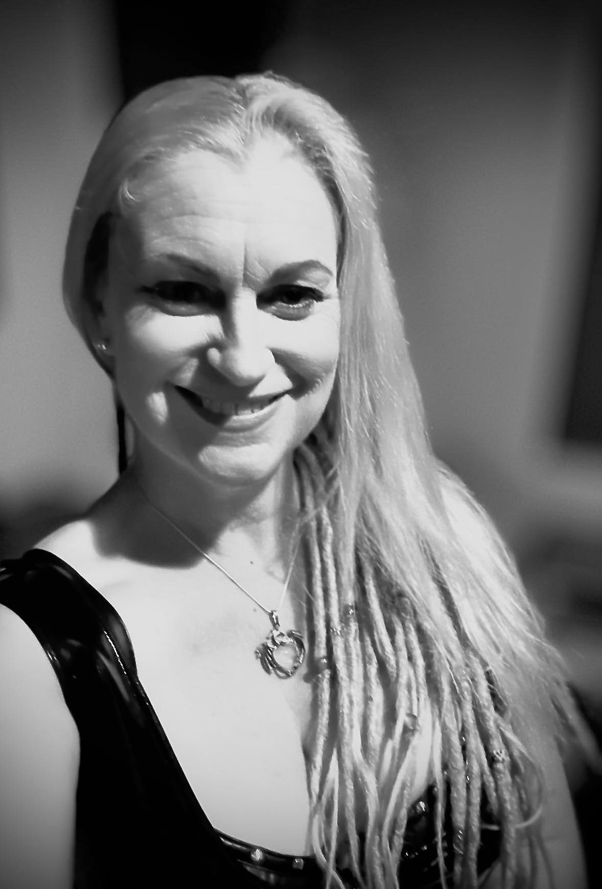 Black and white portrait of a smiling blonde woman with long hair wearing a necklace and dark top.