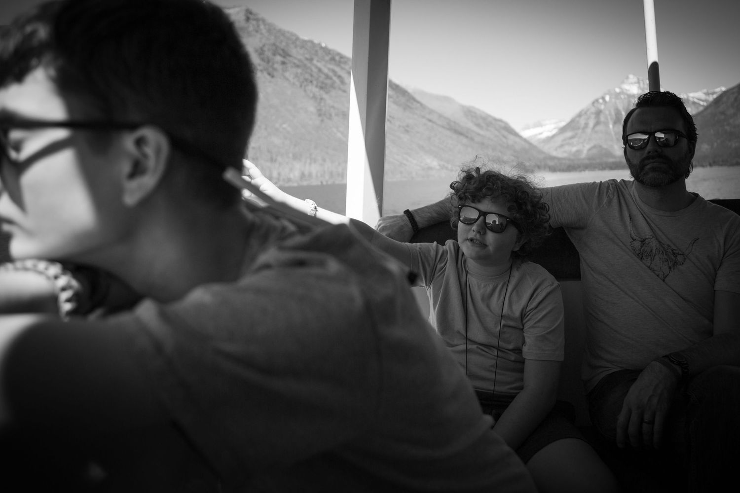 Black and white photo of three people relaxing on a boat with mountain scenery in the background.