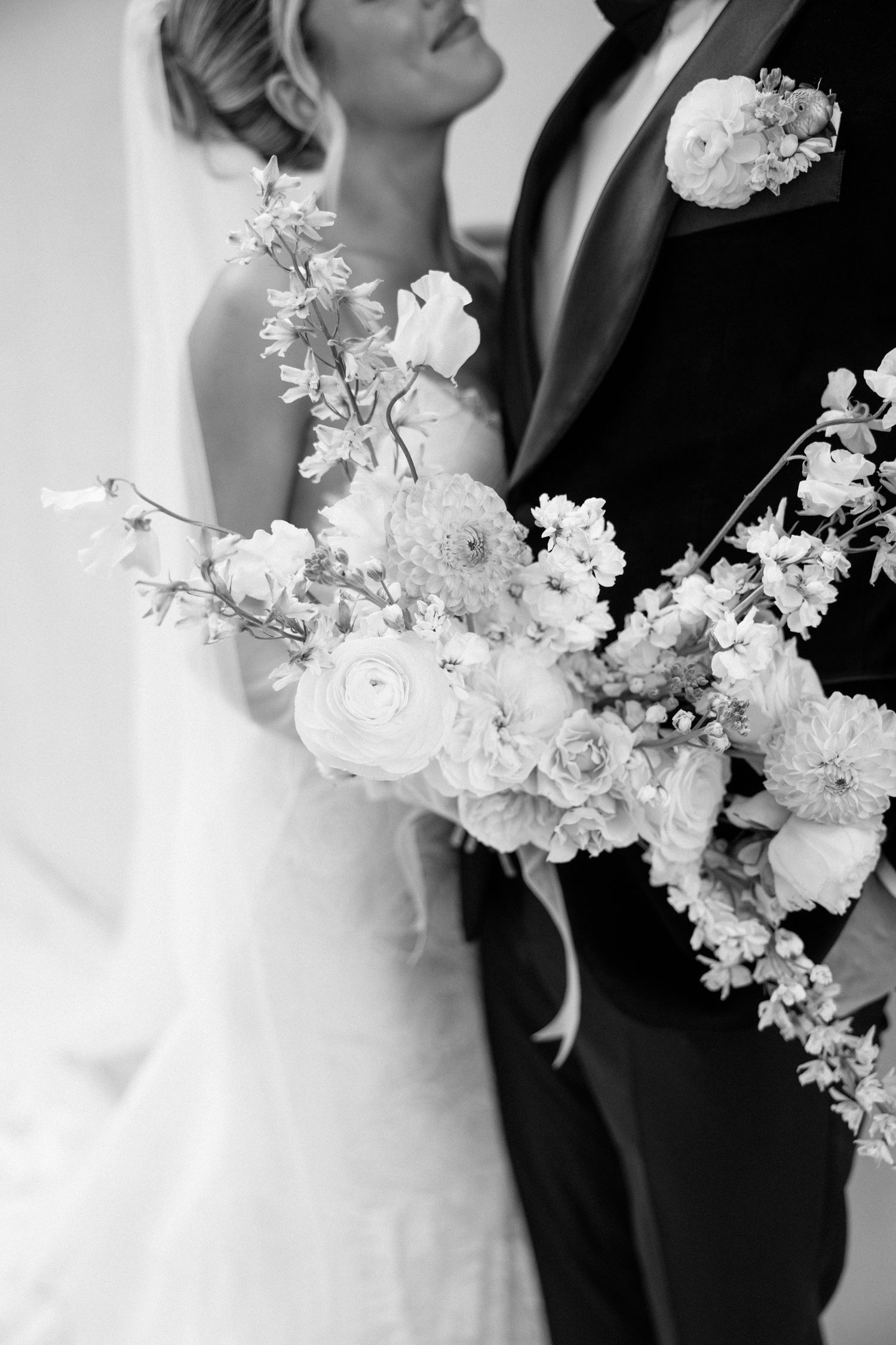 Black and white wedding photo showing bride and groom embracing with delicate white cherry blossoms in the foreground.