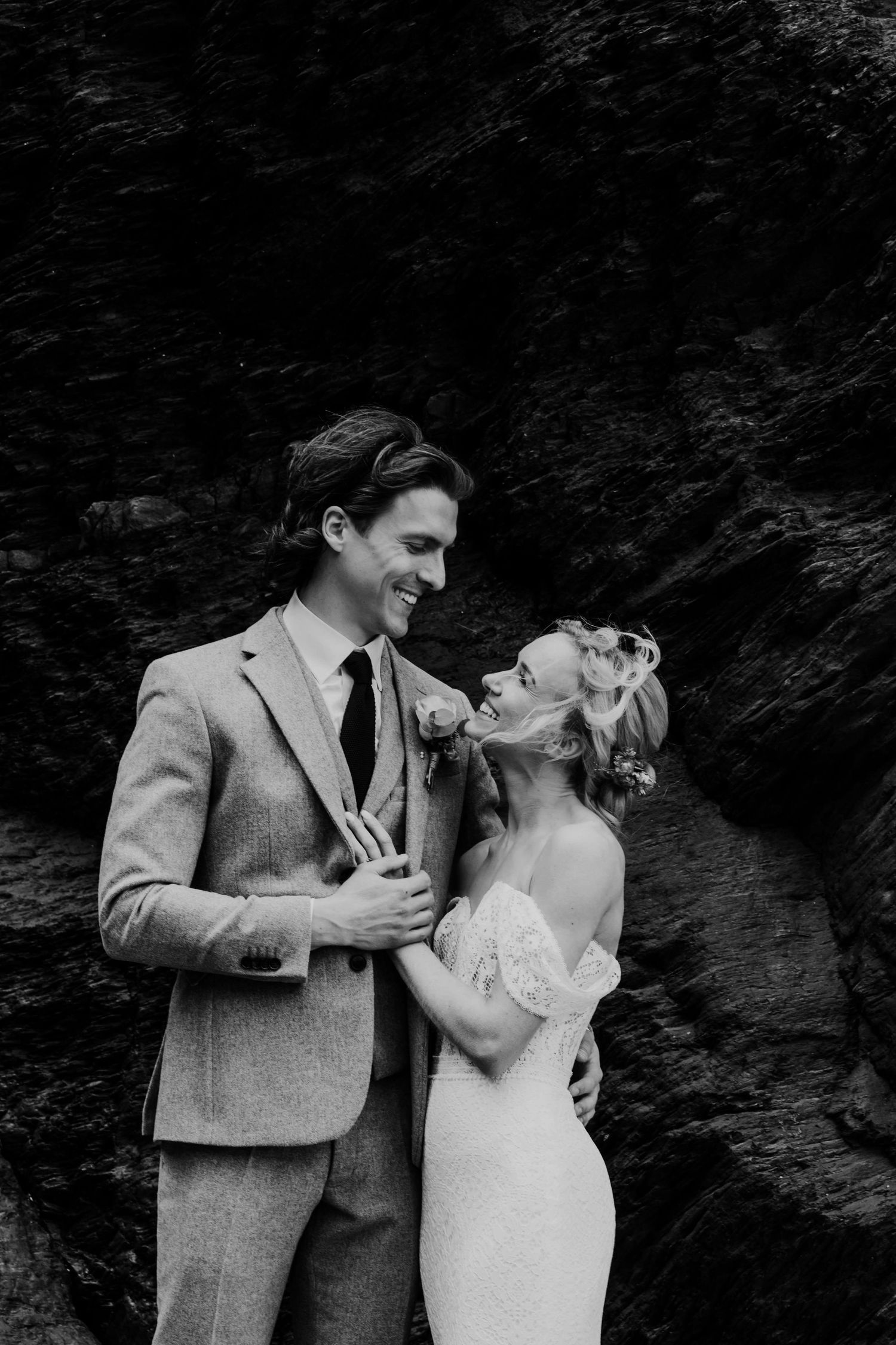 Bride and groom smiling together beside dramatic coastal cliffs on their wedding day.