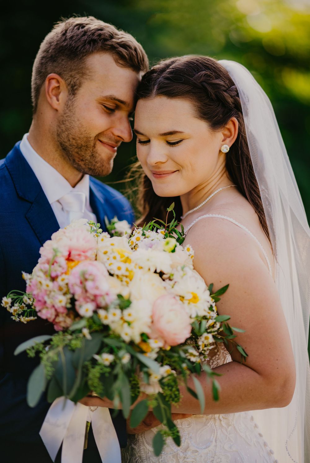 Bride and groom share a tender forehead-to-forehead moment with a pink peony bouquet.
