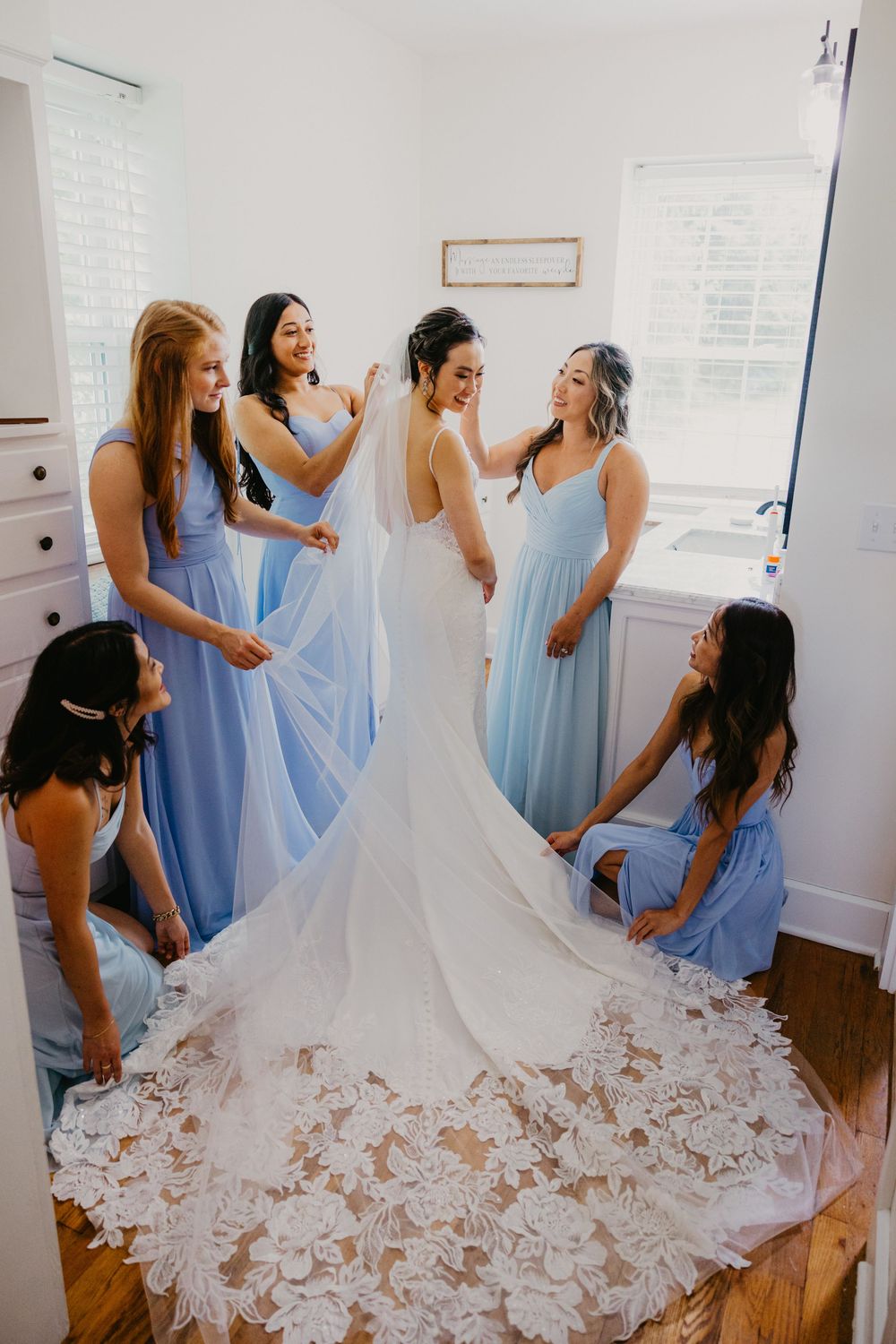 Bride in lace gown surrounded by bridesmaids in blue dresses during wedding preparations.
