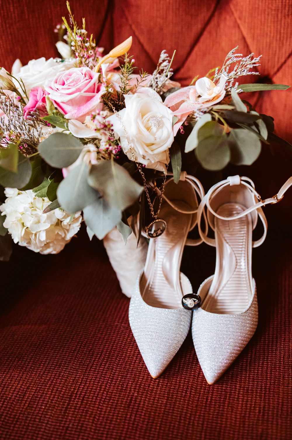 Sparkly pointed-toe bridal heels displayed beside a pink and white rose wedding bouquet.
