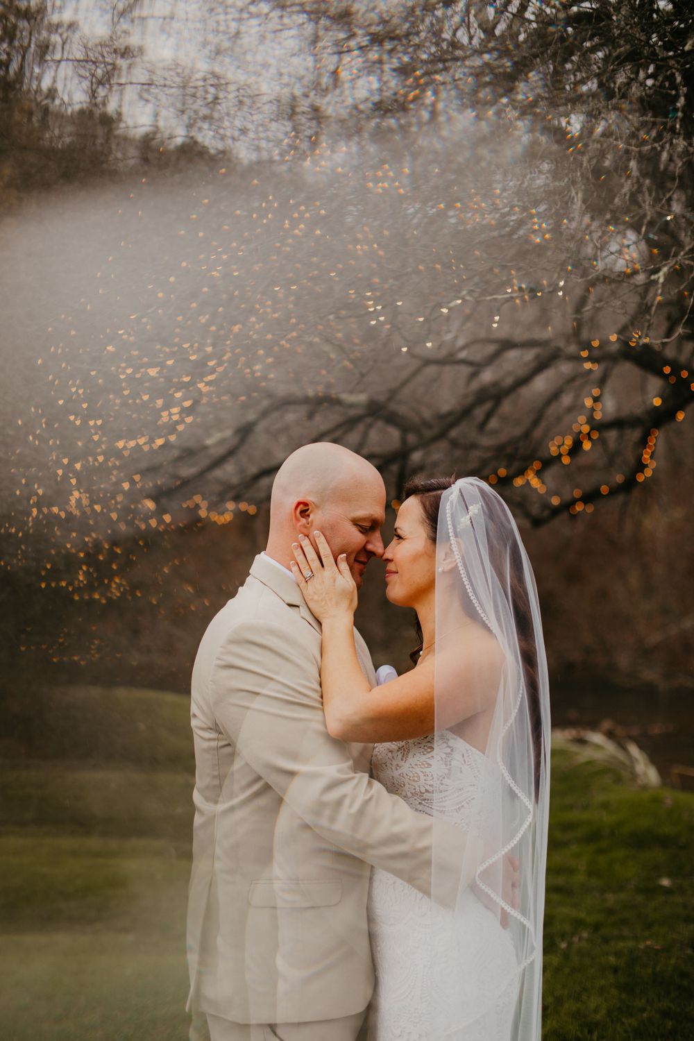 A bride and groom share a romantic forehead-to-forehead moment outdoors, surrounded by misty golden light and autumn trees.
