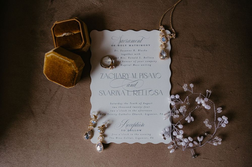 Elegant wedding invitation suite with gold velvet ring box, pearl earrings, and floral hair piece on neutral background.