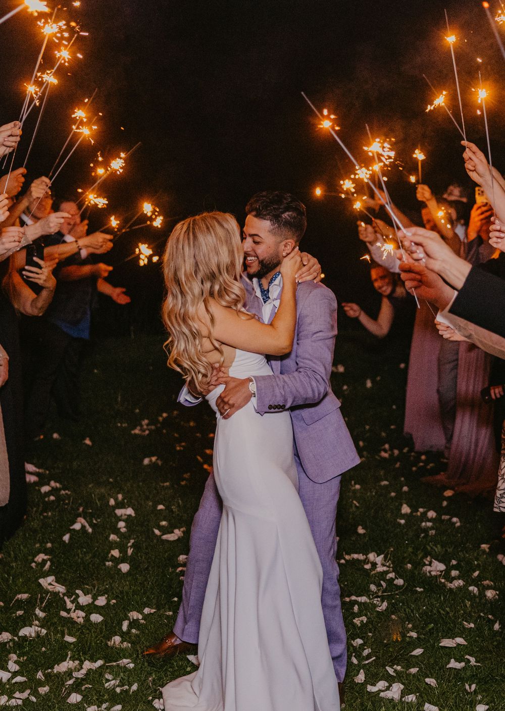 Bride and groom share a romantic kiss during a sparkler send-off at their outdoor evening wedding celebration.