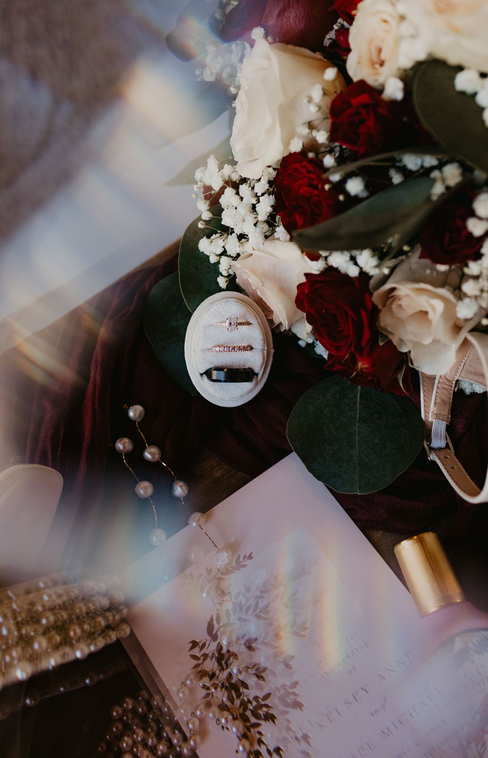Wedding rings in a velvet box surrounded by red and white roses, eucalyptus, baby's breath, and pearl accents.