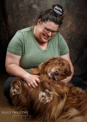 A smiling woman in a green shirt cuddles with a happy golden retriever dog during a professional studio photo session.