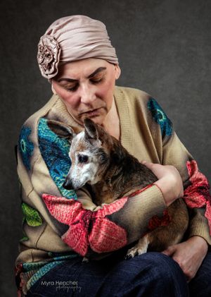 Woman wearing a head wrap tenderly holds a small senior dog while seated in a studio portrait.