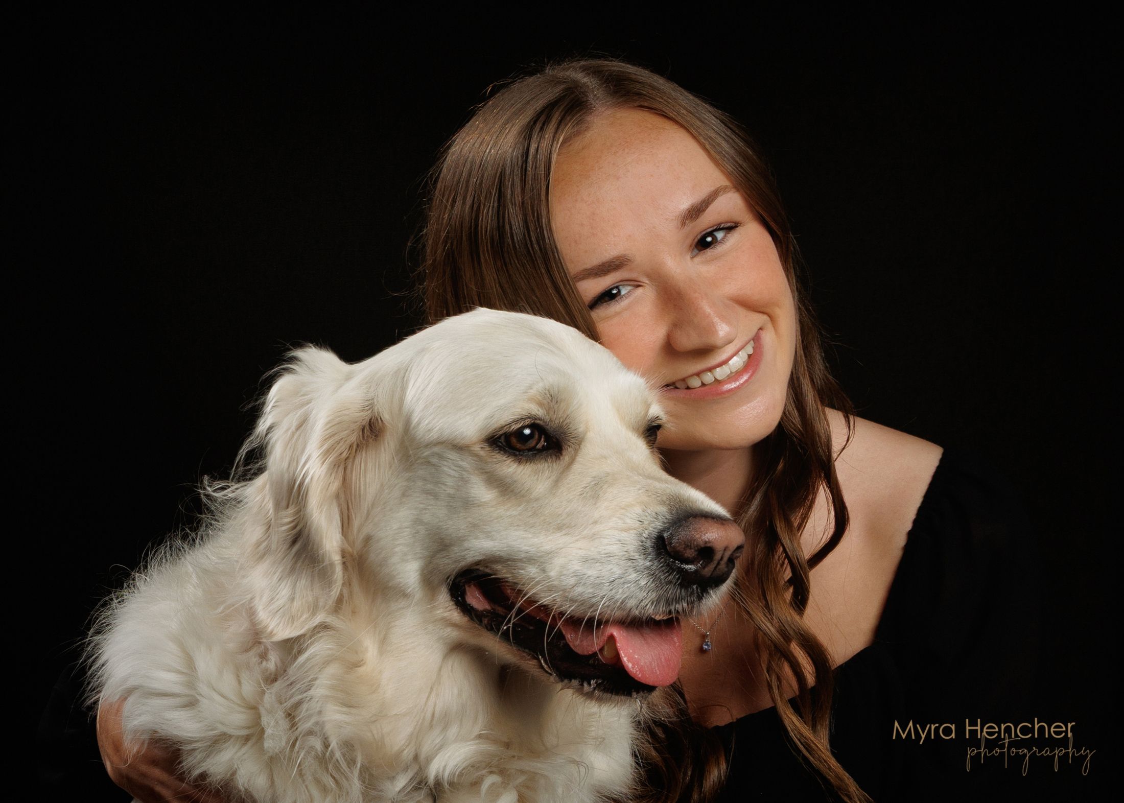 Smiling teenage girl posing with a white Golden Retriever dog against a black studio background.
