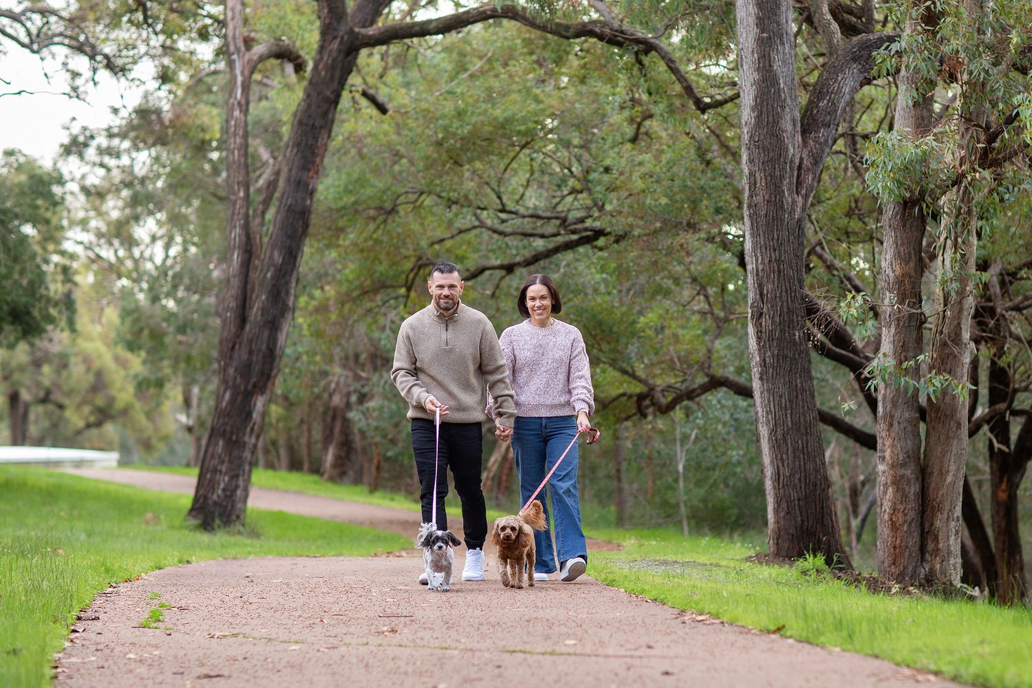 Couple going for a walk amongst tall trees with two cavoodles during pet session in Perth