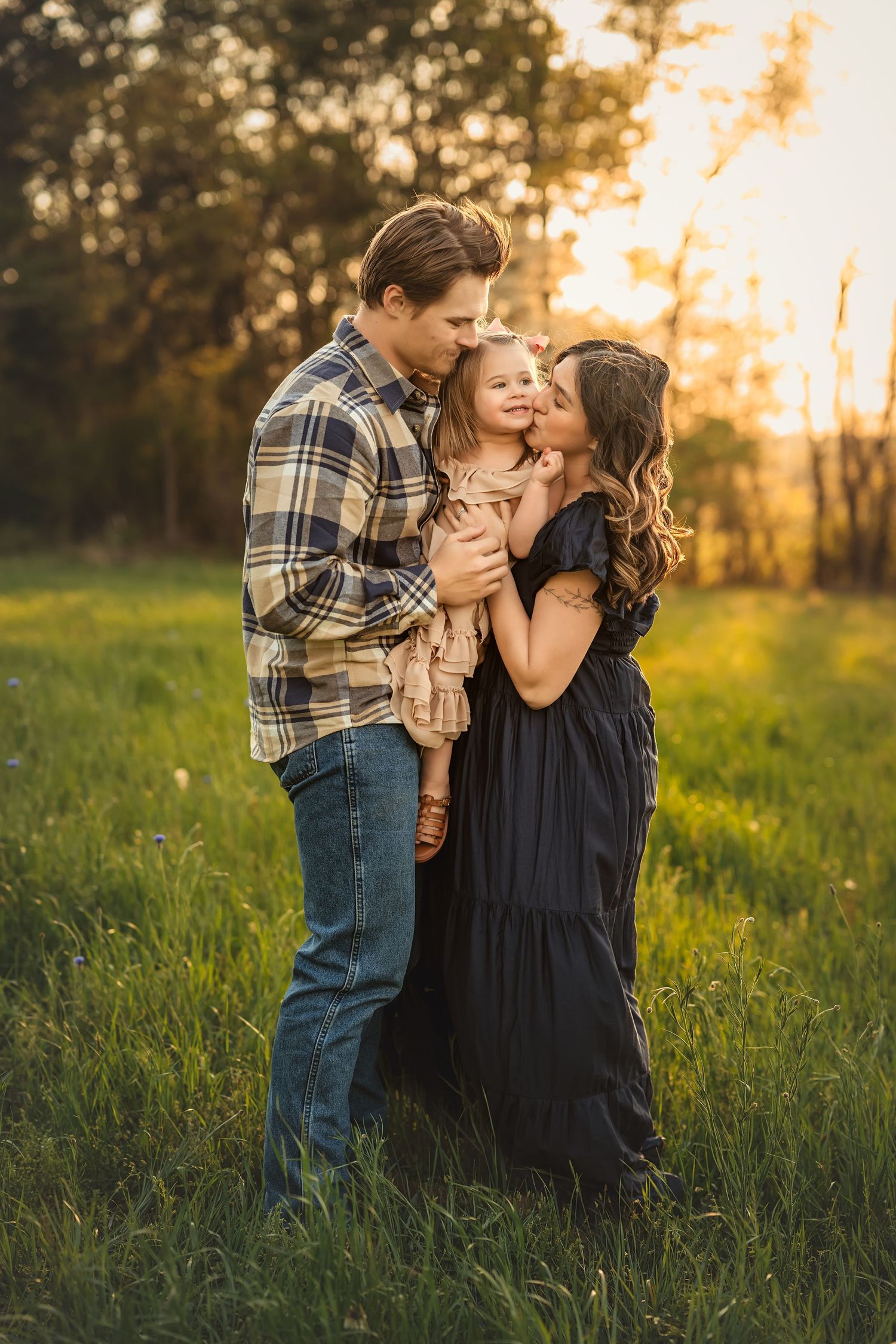 A family embraces together in a field at sunset while wearing casual clothing and sharing an intimate moment.