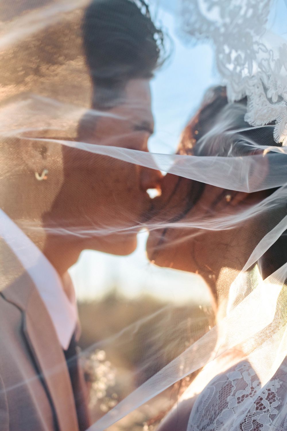 Bride and groom kiss behind the bride's veil.