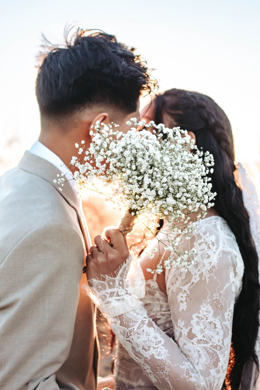 Bride and groom kiss, covered by wedding bouquet.