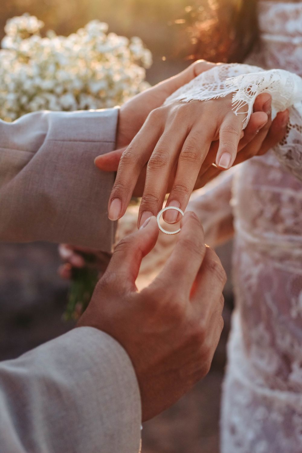 Groom places ring on brides finger with wedding bouquet in background.