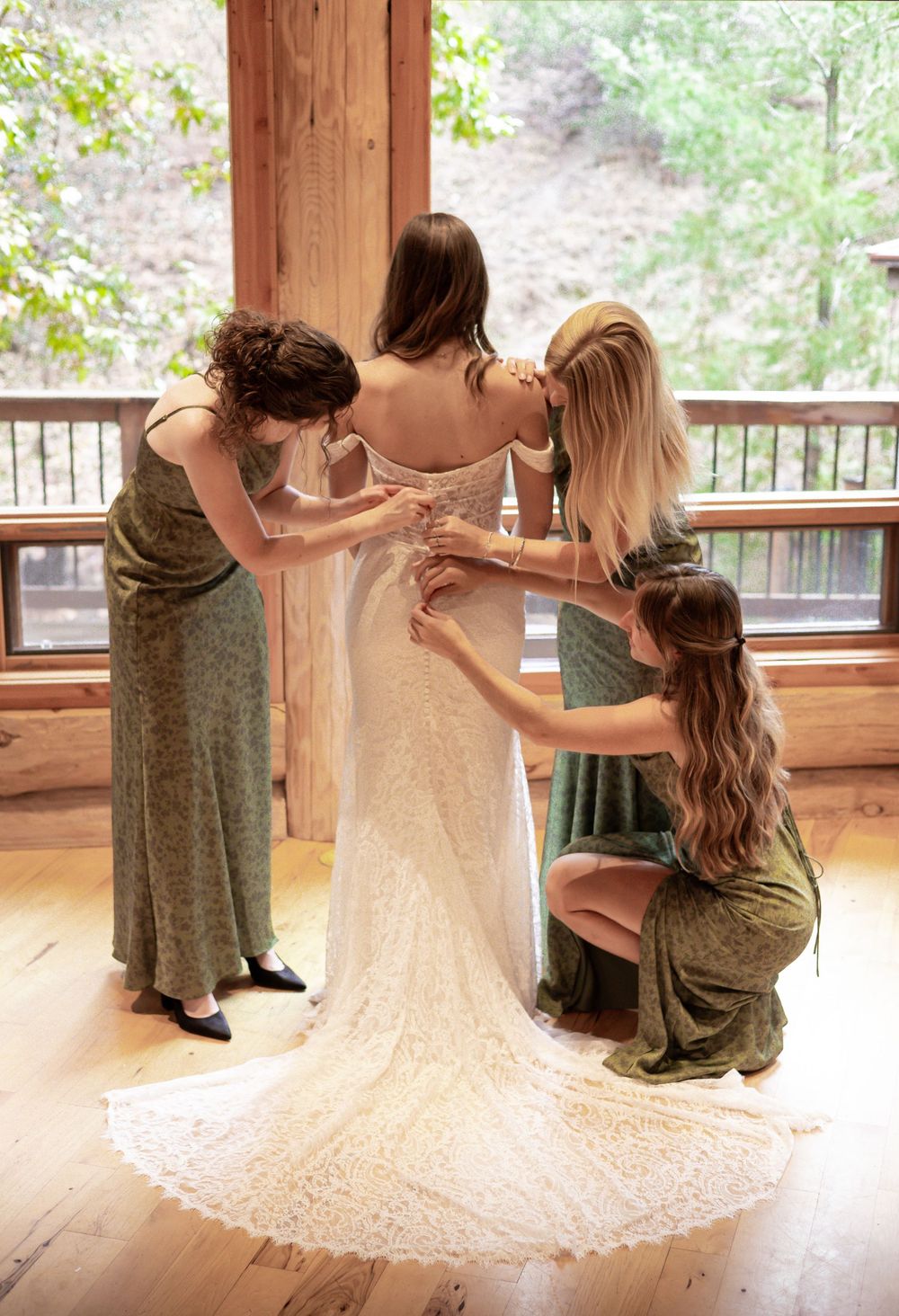 Bridesmaids help bride button up her wedding dress in a golden glow home.