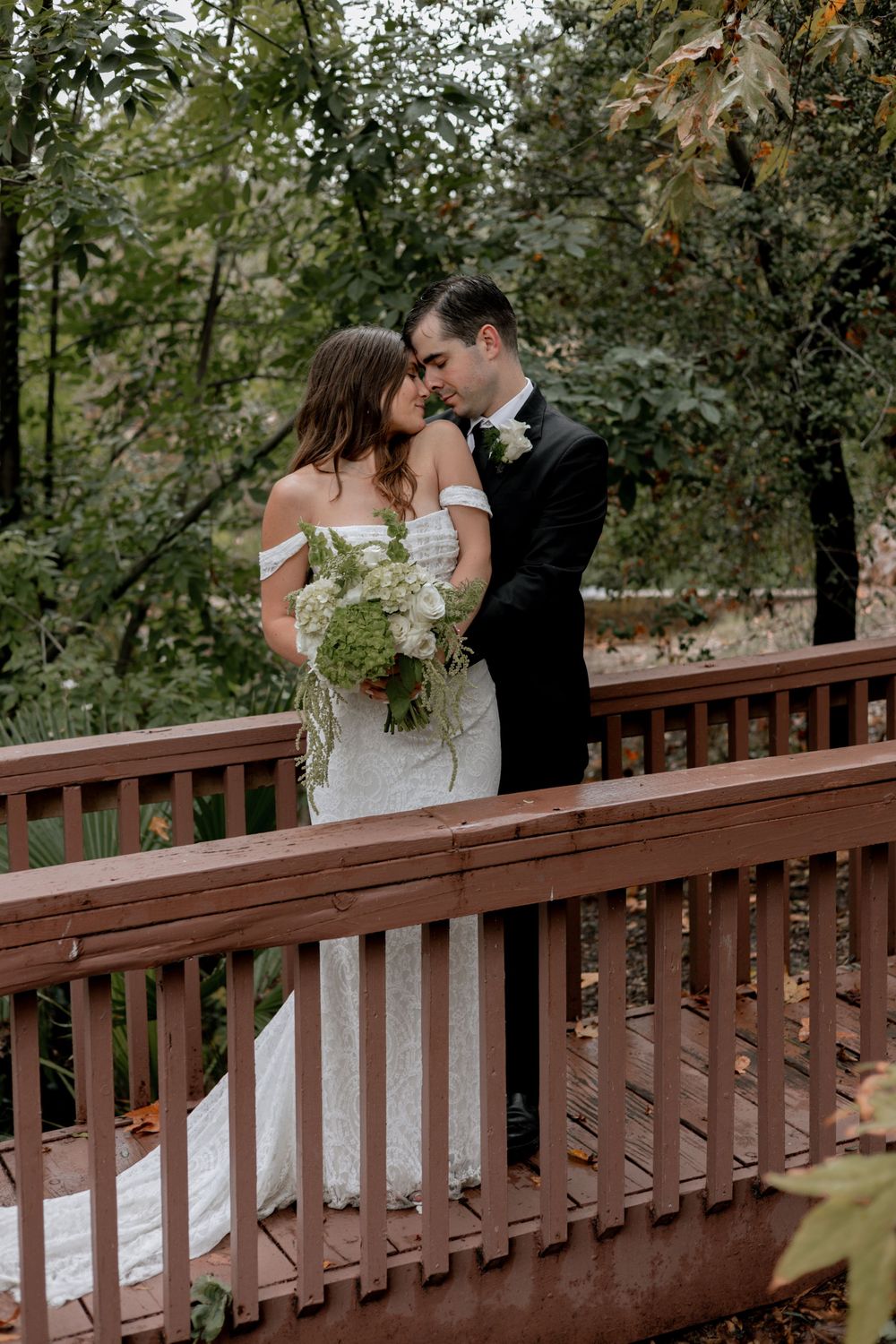 Bride and groom gaze at each other lovingly while standing on a bridge in the middle of a forest.