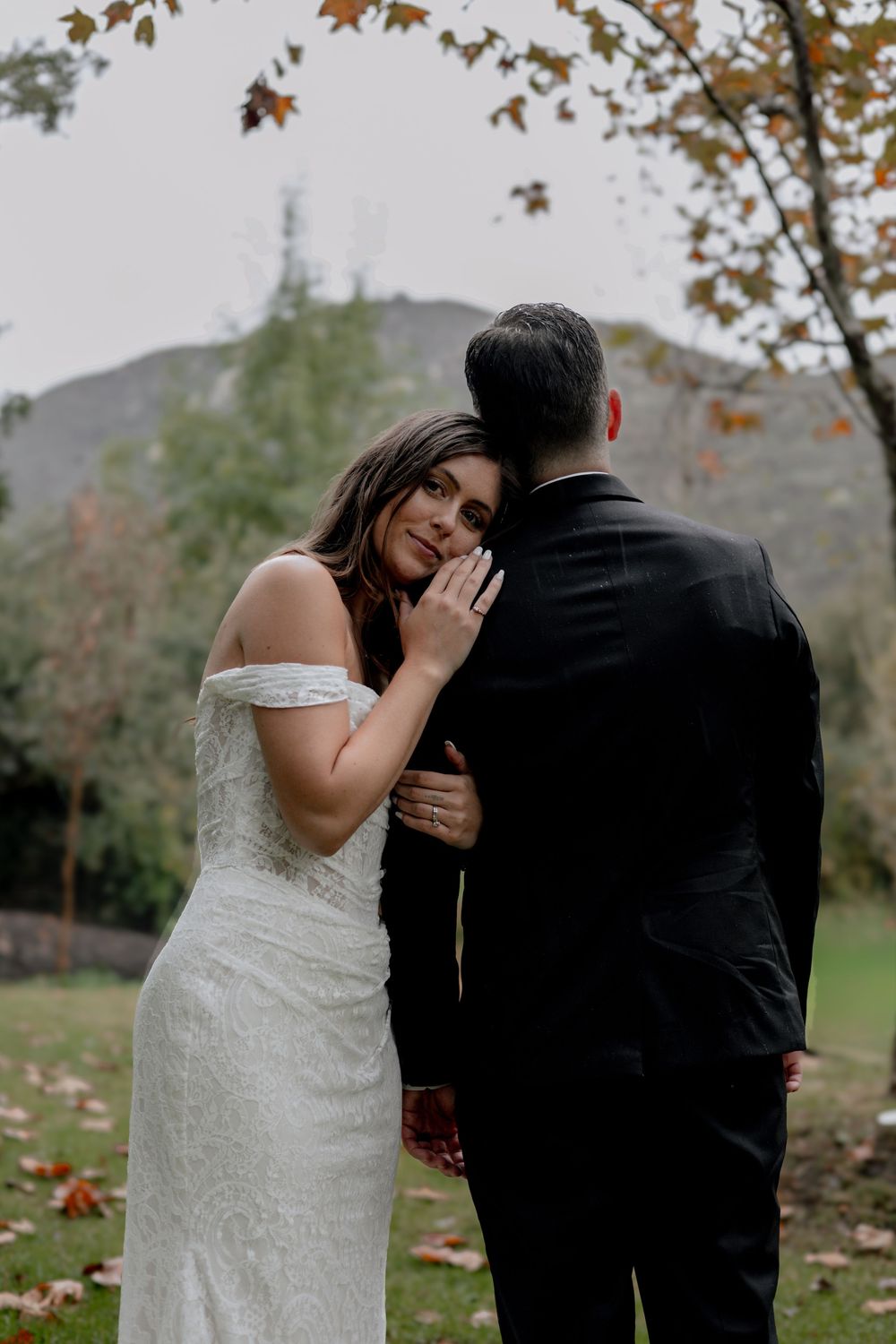 Groom faces away at the forest while bride rests head on his shoulder and smiles at camera.