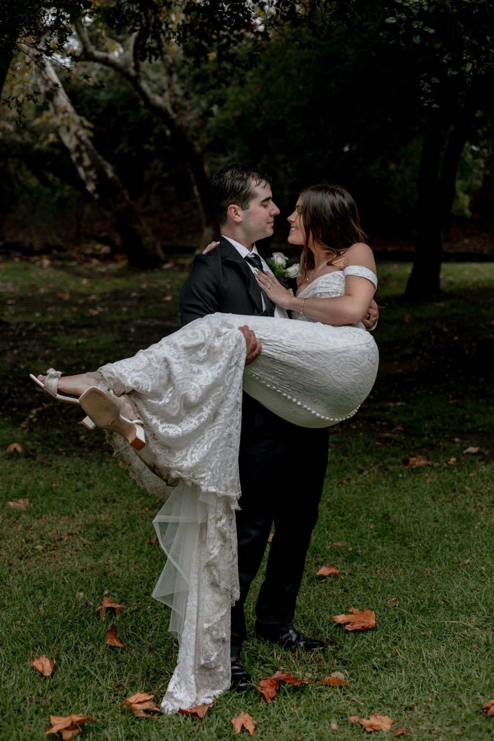 Groom holds bride amidst an orchard of trees.