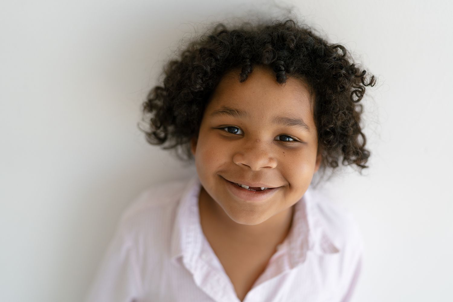 Adorable young child with curly hair smiling brightly against a white background.