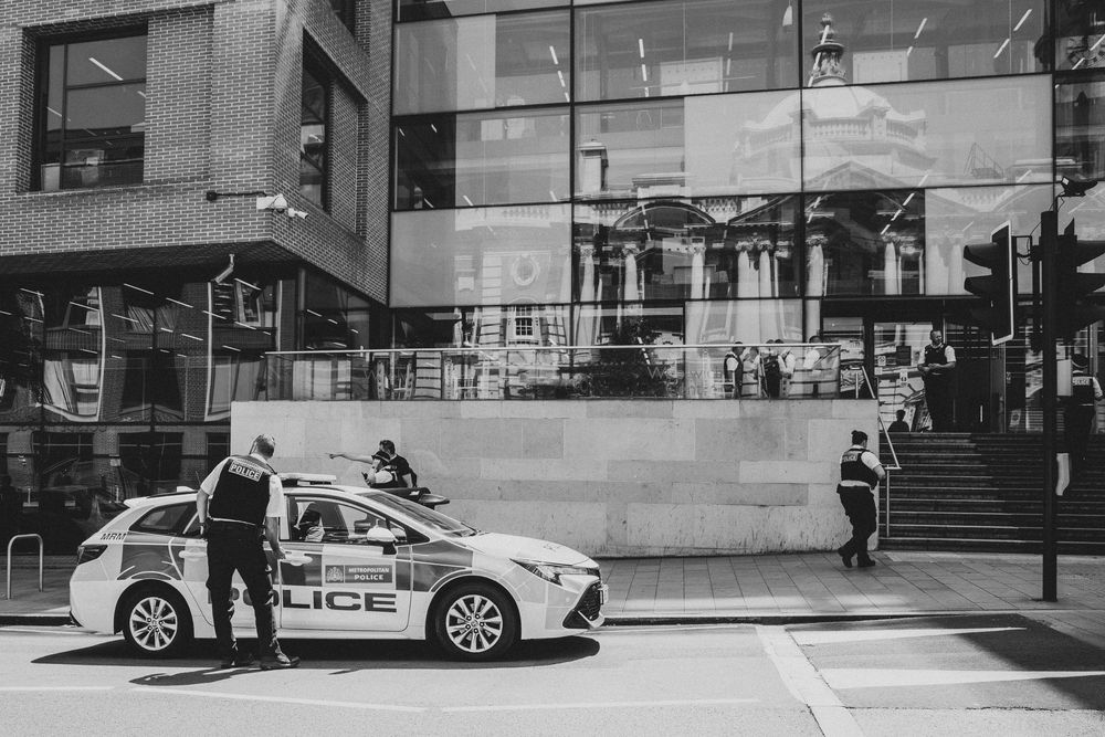 Black and white photo of police car and officers outside a modern glass building in London city street.