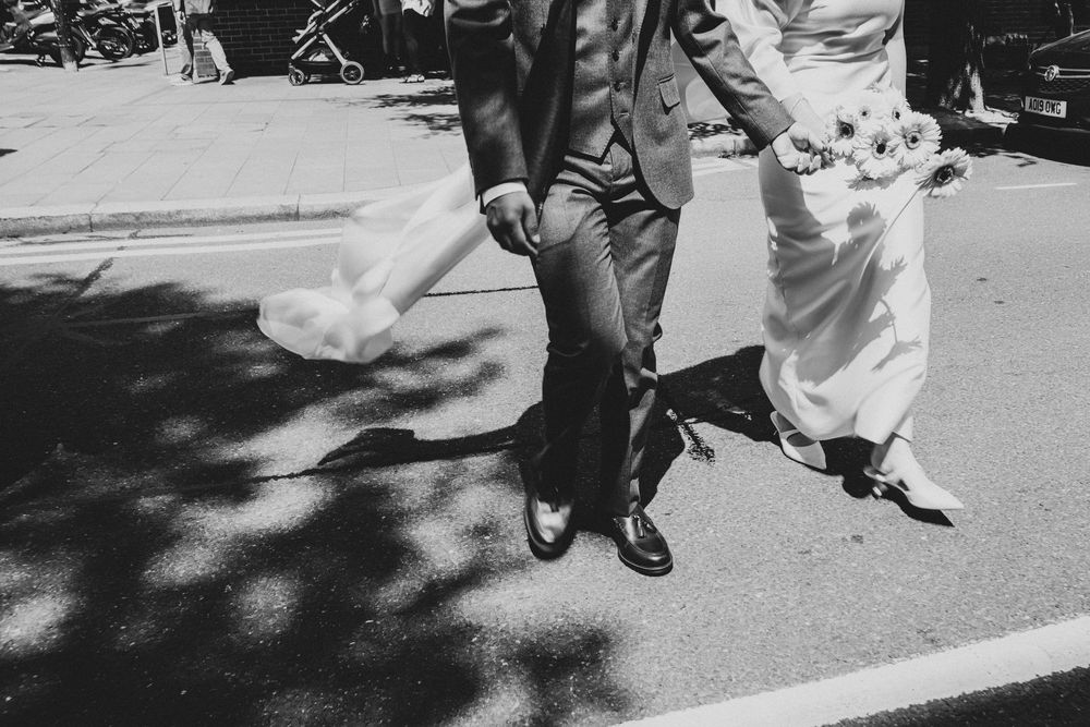 Black and white photo of a bride and groom walking hand in hand in the streets of London, bride holding a bouquet.